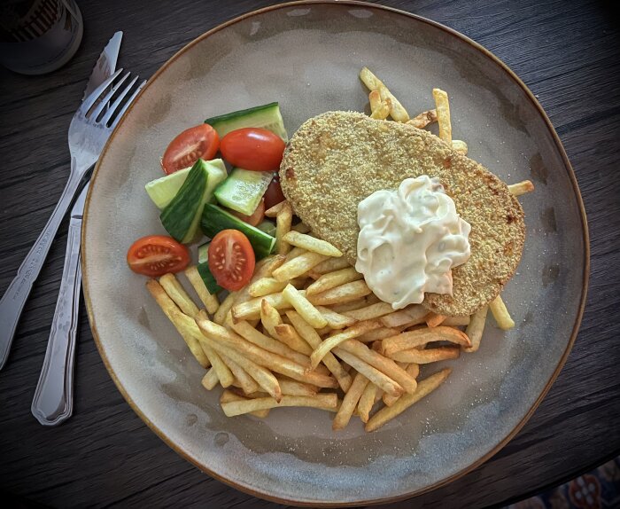 Tallrik med schnitzel, pommes frites, gurka, tomater och bearnaisesås.