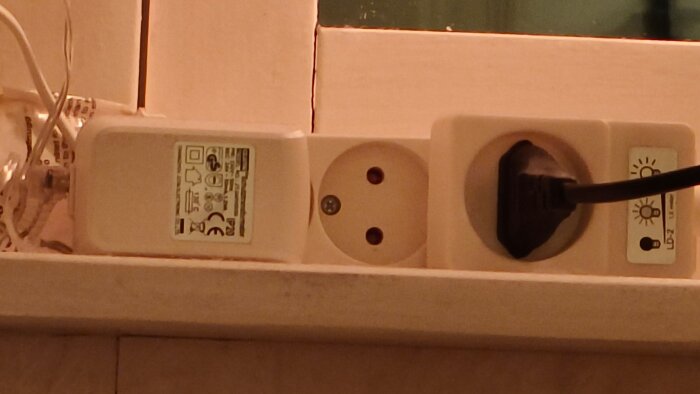 Förlängningssladd, adapter och ansluten eurokontakt i ett eluttag på en fönsterbräda.
