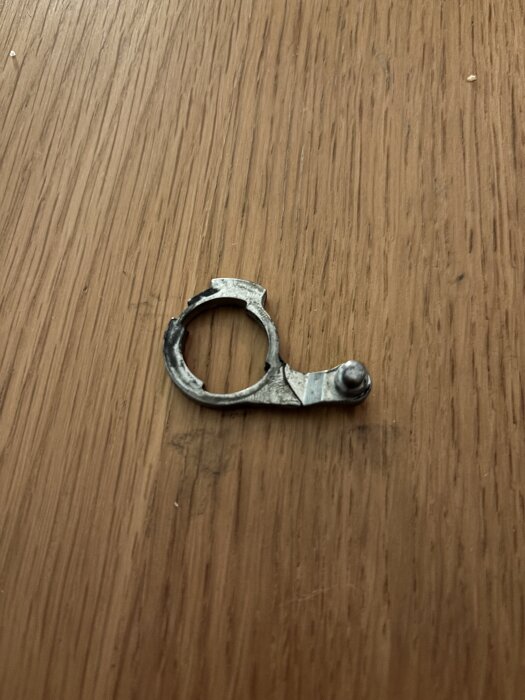 Trasig metallkomponent från låskista ligger på ett träbord.
