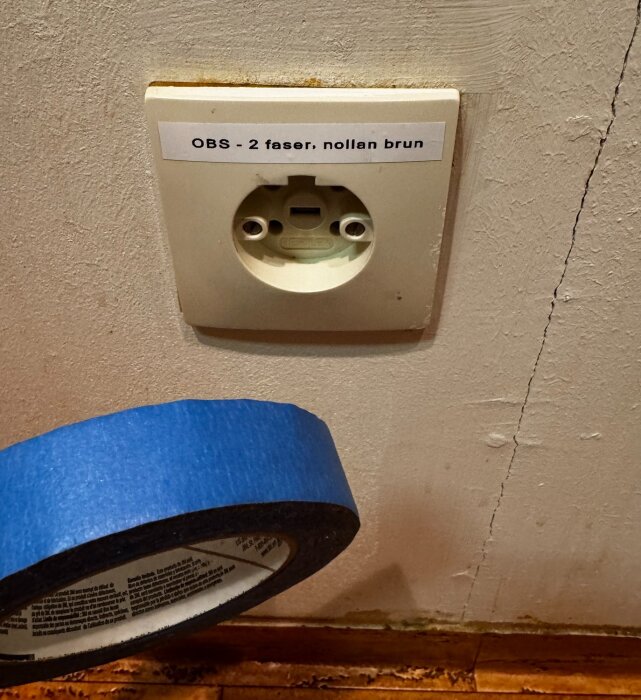 Vägguttag med perilexanslutning, märkning "OBS - 2 faser, nollan brun", och en rulle blå tejp vid sidan av.