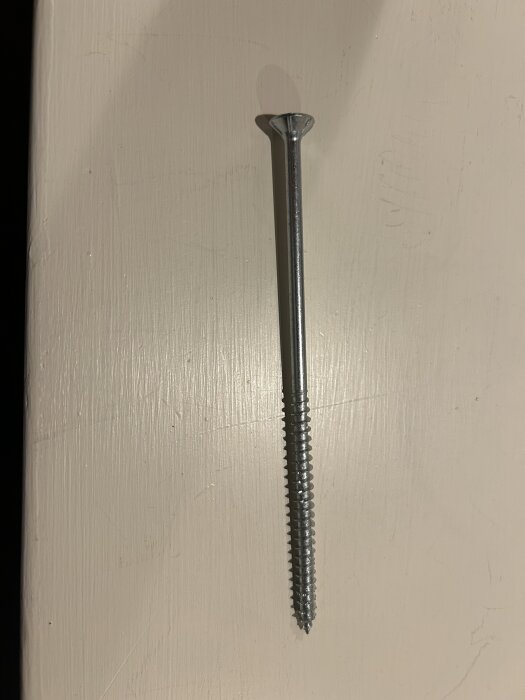 En lång metallskruv avsedd för att hänga en tung spegel på en tegelvägg.