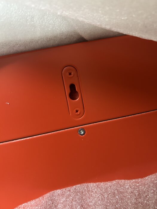 Orange panel med nyckelhålsfäste och en skruv synlig, omgiven av vadderat material.