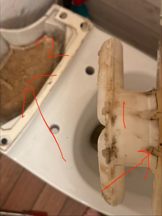Närbild av toalett med isärtagna delar, två röda markeringar visar varmvattenutloppet (1) och porslinsskålen (2), belyser läckagerisk.