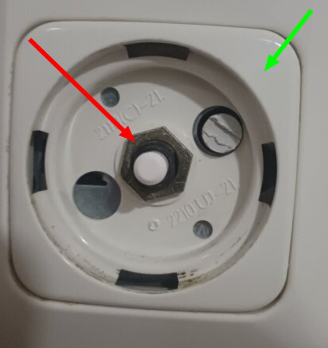 Närbild på en skruvmutter och ett vitt plastlock på en dimmer, markeringar med röd och grön pil som visar skruvens och lockets placering.
