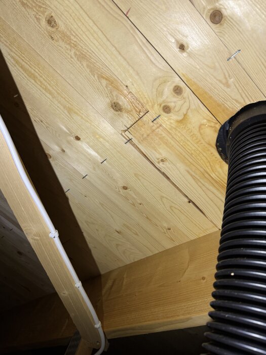 Svart avloppsluftningsrör genom vinden, synlig träkonstruktion och vit kabel.