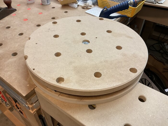 Handgjord Lazy Susan i MDF med flera hål och möbelhjul, placerad på en arbetsbänk i en verkstad.