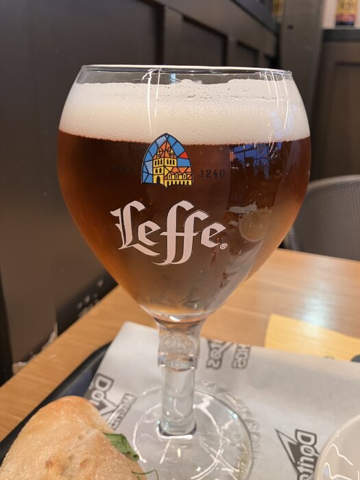 Ett glas med Leffe-öl står på ett bord bredvid en del av en baguette.
