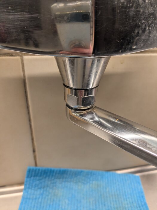 Närbild av ett metallhandtag och en del av en behållare, med en blå tygduk i bakgrunden.