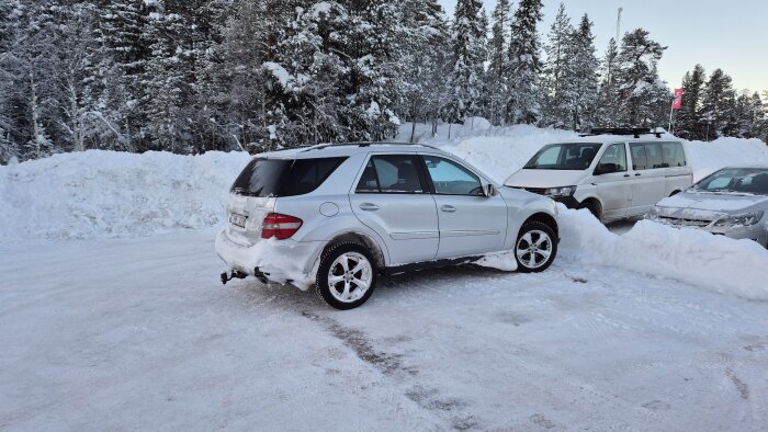 Silverfärgad SUV parkerad i snöigt vinterlandskap med skog i bakgrunden och snöplogade vallar runt omkring.