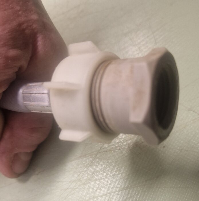 En hand håller i en vit plastkoppling ansluten till en slang, som används för att koppla en diskmaskin.