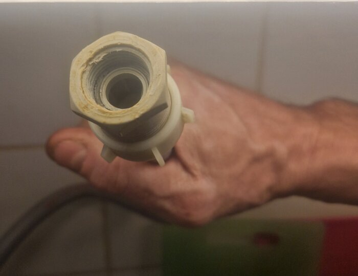 Närbild av en hand som håller i en plastkoppling/slanganslutning som ska passa en diskmaskinskoppling.