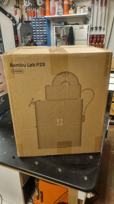Förpackning märkt "Bambu Lab P2S Combo" på ett arbetsbord i ett verkstadsutrymme.