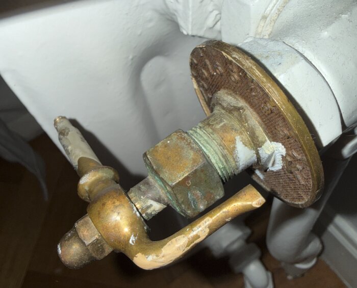 Gammal radiatorventil med avlägsnat vred, nött och stillastående justeringsnål, omgiven av rost och kalkbeläggningar.