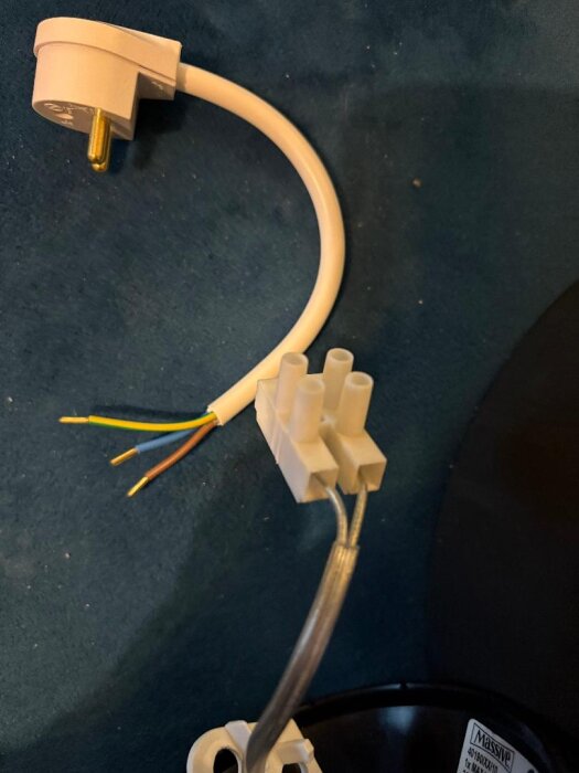 Omonterad taklampa med vit sladd, sockerbit och stickpropp; ofärgade och färgade ledare synliga, mot blå bakgrund.