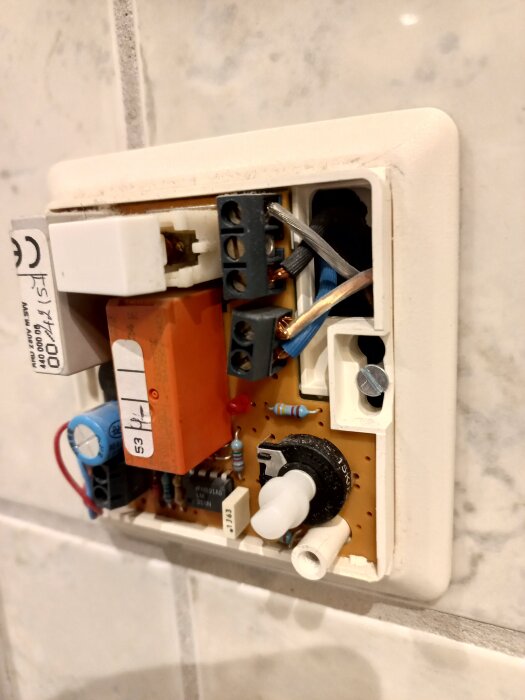 Elektronisk komponent med kretskort och kablar, visas i ett eluttag på väggen.