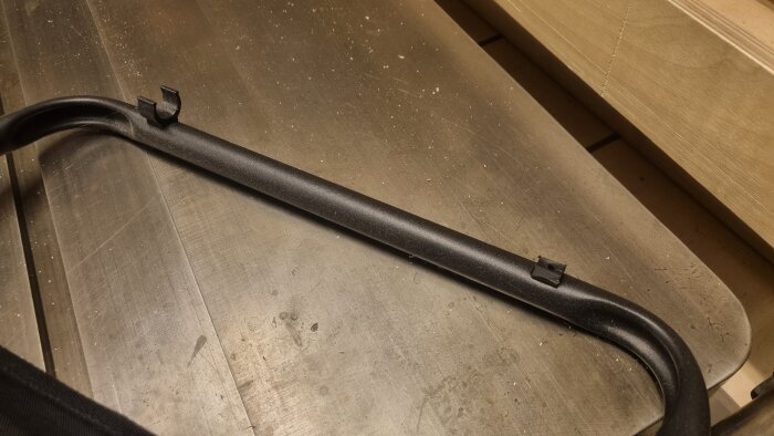 Svart plastkrok för fotpall på husvagnsstol ligger på en metallbänk.