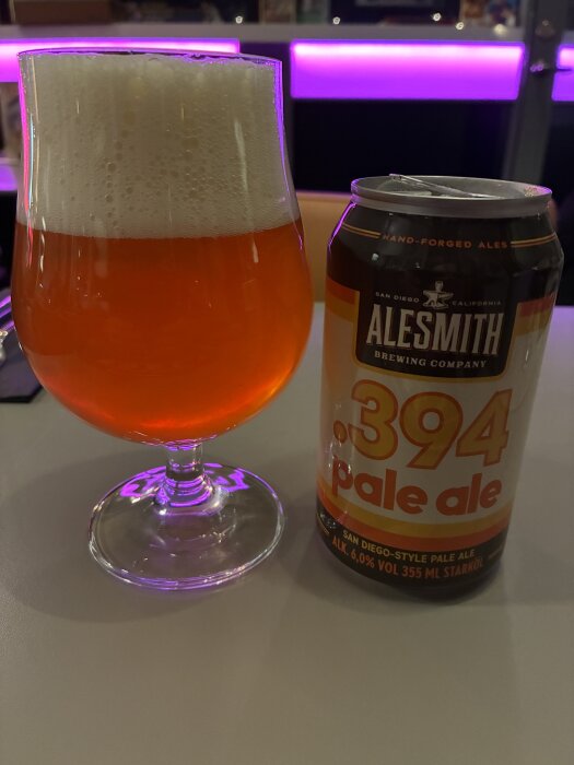 Ett glas öl bredvid en burk Alesmith .394 pale ale på ett bord med lila bakgrundsbelysning.