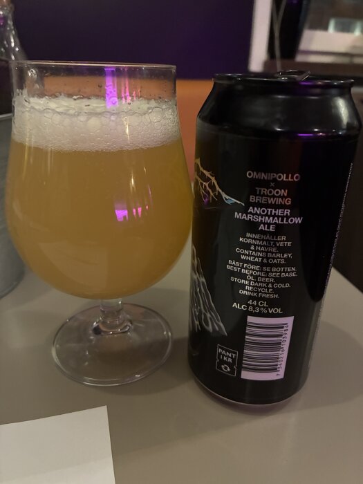 Glas med öl och en burk Omnipollo Another Marshmallow Ale på ett bord.