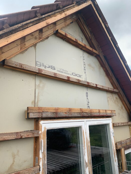 Gavel med exponerad gipsskiva och träregelverk, fönster med flagande färg under renovering av husfasad.