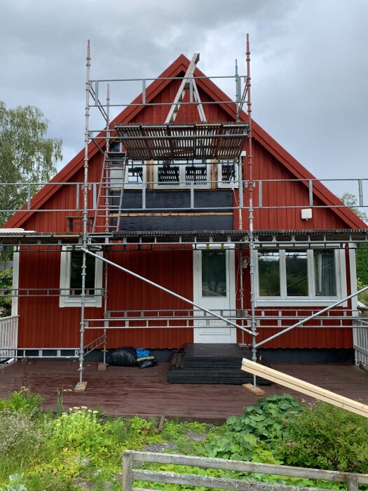 Rött 1.5-planshus med byggnadsställning, nya röda vindskivor, och pågående renovering av fasad och tak, med utbyte av panel och isolering.