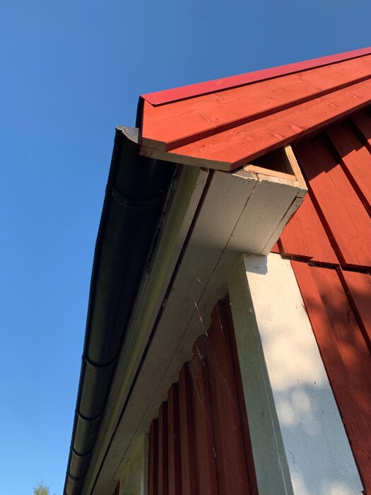 Röda vindskivor på ett hus med nyrenoverad fasad och tak, sett underifrån mot en klar blå himmel.