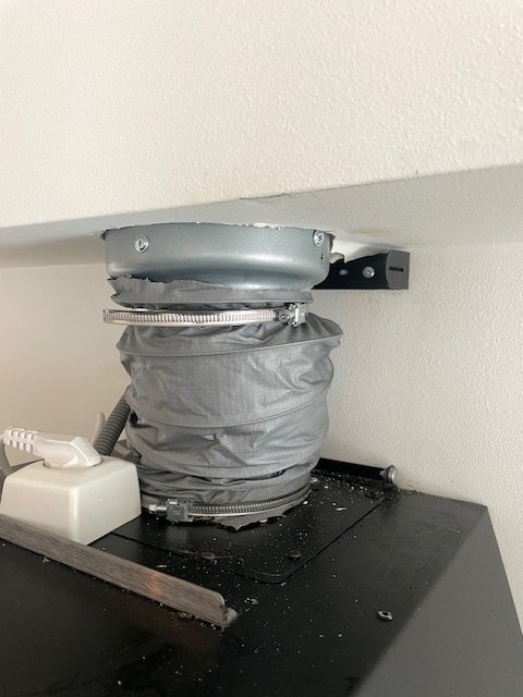 Flexibel ventilationsslang ansluten mellan köksfläkt och imkanal. Slangen är hoptryckt, med metallfästen och reduktion till mindre dimension.
