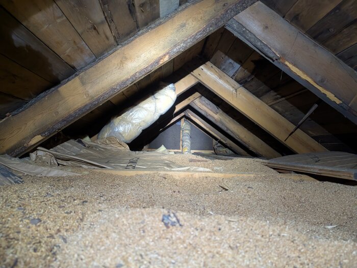 Vind med sågspånsisolering och synliga takstolar. Bristfällig ventilation med isolering direkt mot råsponten och svarta fuktfläckar på träet.