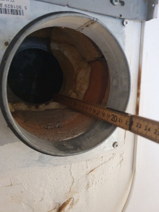 En mätsticka visas i en köksventilationens metallrör, omgiven av isoleringsmaterial. Detta illustrerar installationsproblemet.