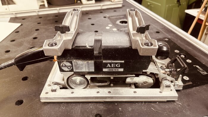 AEG HBSE 75 S bandslipmaskin med bordsfästen och svart handtag, placerad på en verkstadsbänk.