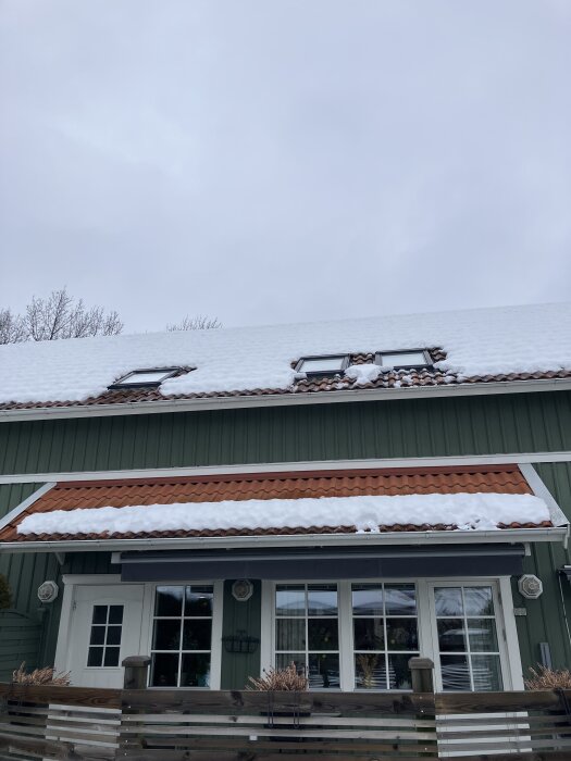 Tre takfönster på ett snötäckt tak med ett litet skärmtak nedanför, snö delvis borttagen ovanför varje takfönster.