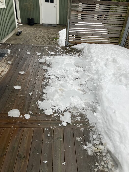 Snötäckt träaltan med isblock som fallit från taket. Snö ligger mot ett plank, antyder behov av snörasskydd.
