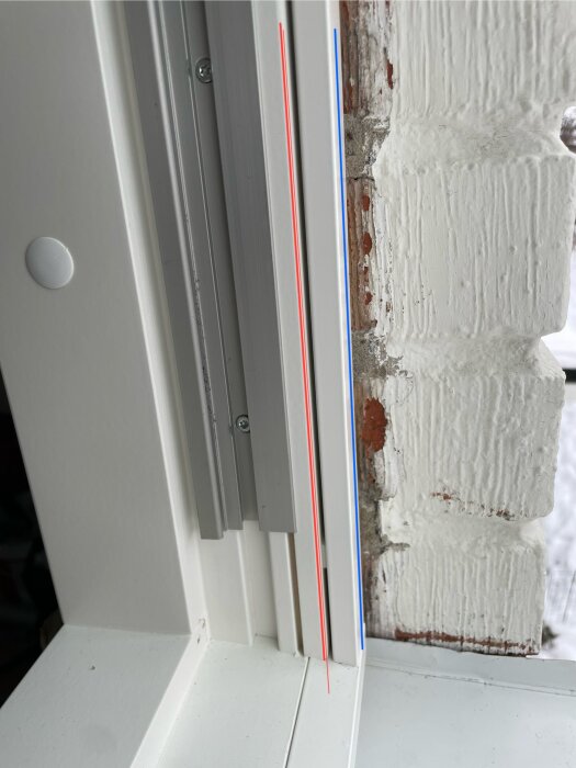 Vridfönster monterat i en tegelvägg, med röda och blå linjer som markerar karm och aluminium, samt springa för ventilation.