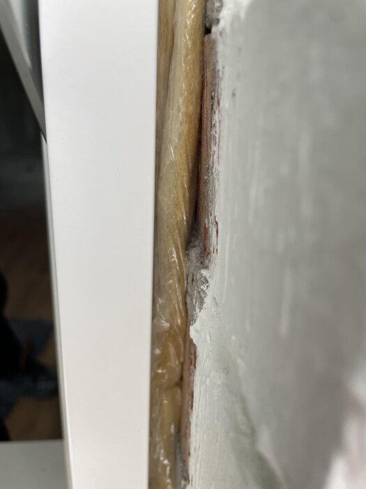 Närbild av monterat trä-aluminiumfönster mot tegelvägg med fogning och drev; vit karm och en smal ventilationsspringa syns.