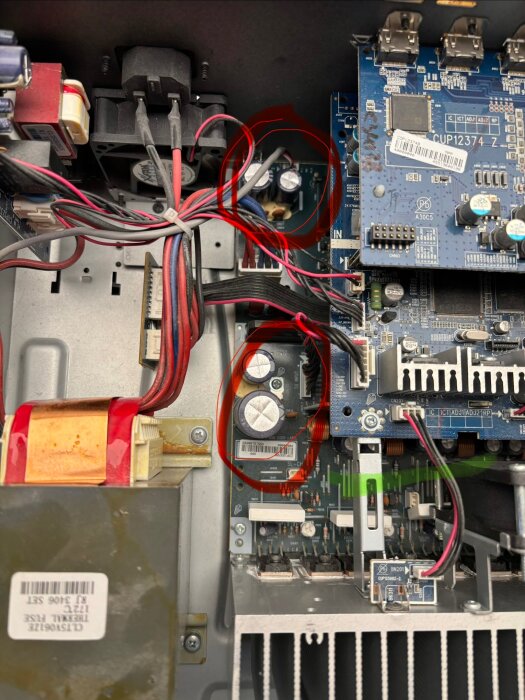 Närbild av insidan på en receiver med flera kondensatorer markerade med rött. Kondensatorerna har ett vitt material runt sig.