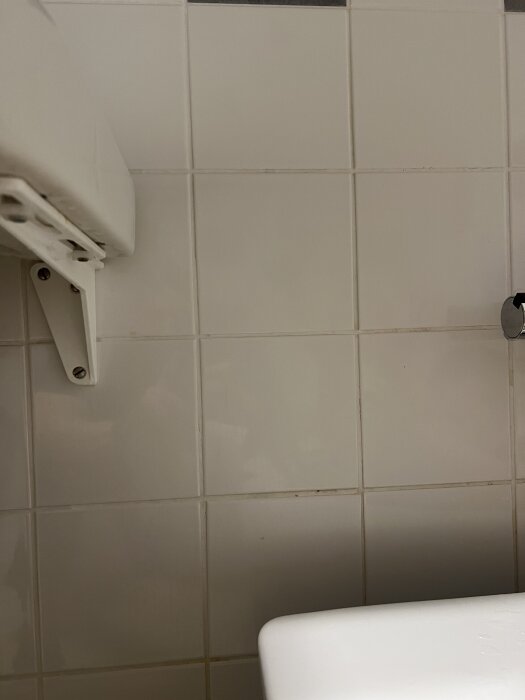 Kaklad vägg i badrum med synlig kant av handfat och fäste för väggarmatur, avsedd för montering av en badkarsvägg i glas.