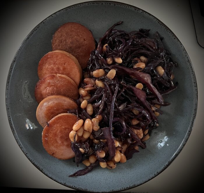 Stekta korvskivor med bönor i tomatsås och fräst rödkål på en tallrik.
