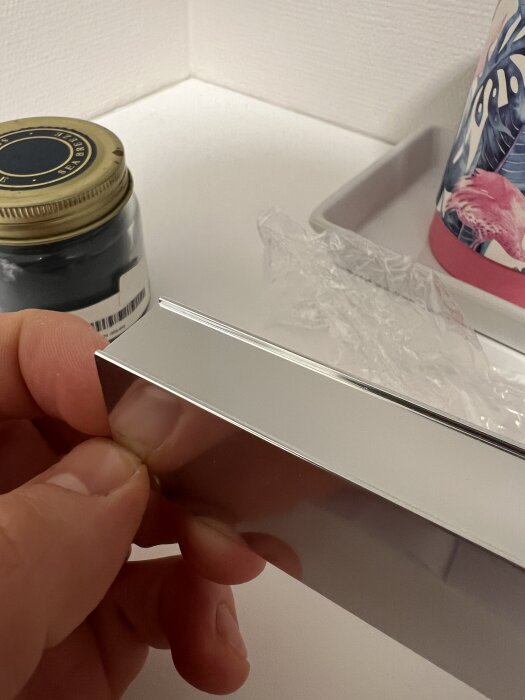 Närbild på en person som håller ett kromat väggfäste för glaspanel, med fokus på fästytan.