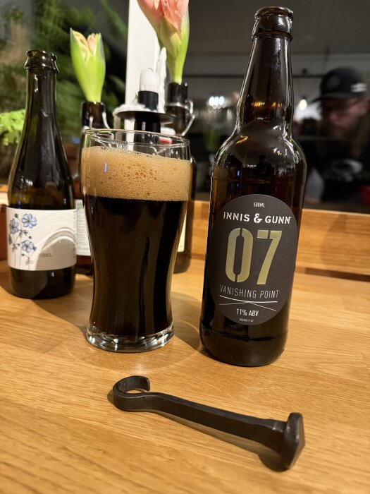 Flaska och glas med Innis & Gunn Vanishing Point 07-stout på ett träbord, bredvid en kapsylöppnare.