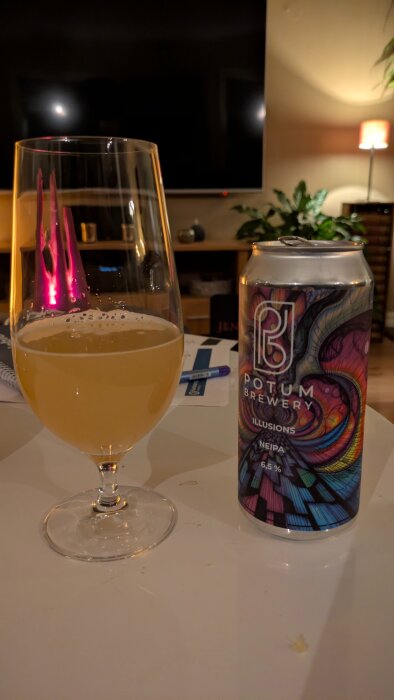 Ett glas med ljus öl bredvid en färgglad burk från Potum Brewery på ett bord, i ett mysigt upplyst rum.