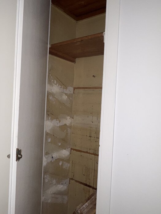 Ett tomt skafferi med borttagna hyllor och märken på väggarna där spackling behövs innan målning.
