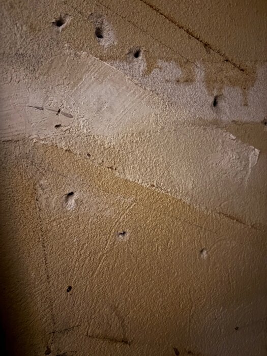 Vägg med hål och spår efter hyllor i ett skafferi, redo för spackling och målning innan nya hyllor sätts upp.