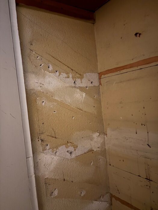 Vägg i skafferi med borttagna hyllor, märken och spackelrester, redo för vidare behandling och ny installation.