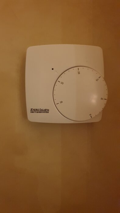 Termostat monterad på en vägg med märke EnergiJagarnas golvvärmesystem, inställd på cirka 23 grader Celsius.