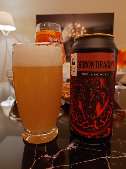 En glas med ljus öl bredvid en svart burk med rött demon-dragon motiv och texten "Doble Neipa 8%".
