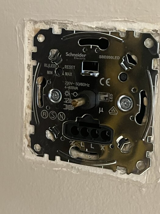 Närbild av en Schneider Electric dimmer inmonterad i väggen, med synliga anslutningar och skruvar.