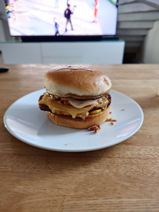 Cheeseburgare på en vit tallrik framför en tv, stående på ett träbord.