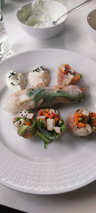 Vårrullar med kyckling, morot, sparris och röd peppar på en tallrik, serverade med två såser av skyr, en med wasabi och en med tahini och chilisås.