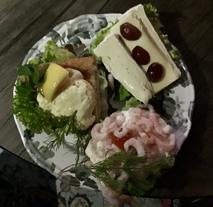 Tre smörrebröd på en tallrik, med räkor, lax, spätta, rostbiff och brie med vindruvor, dekorerade med sallad och citron.