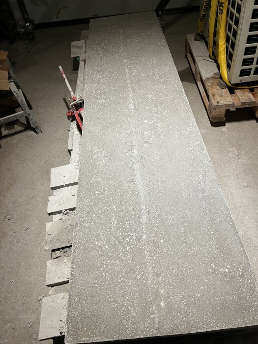 Betongskiva på arbetsstation omgiven av verktyg och material, som stadigt vilar ovanpå ytan. Ljus reflekterar mjukt över dess skrovliga textur.