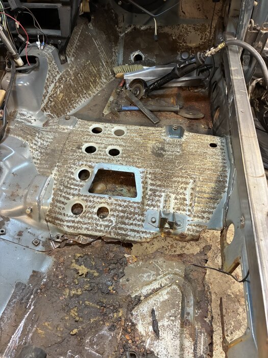 Reparerad interiör av en gammal bil, rostiga delar och verktyg syns, kanske en Volvo 240 under renovering.